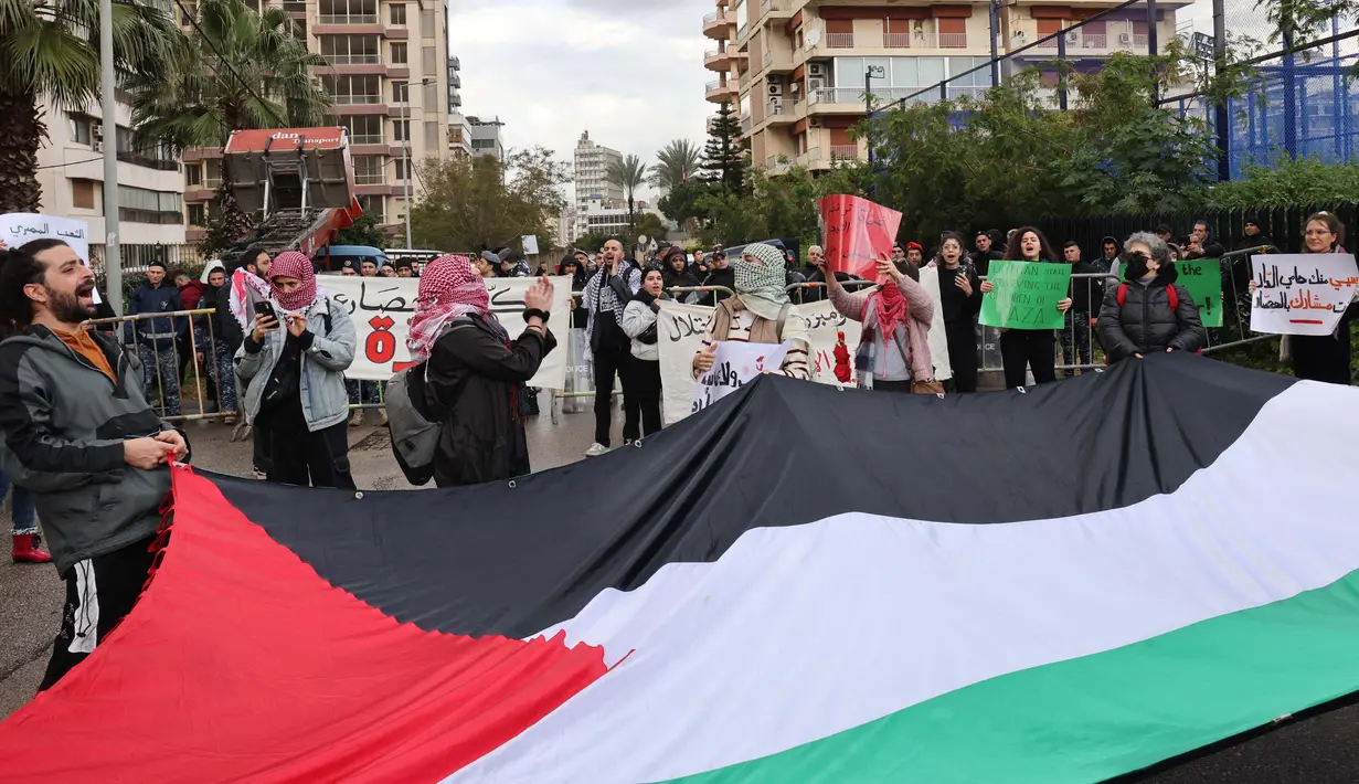 Para aktivis memegang bendera Palestina raksasa dan menutup jalan menuju kedutaan besar Mesir di ibu kota Lebanon, Beirut, pada 19 Februari 2024. (ANWAR AMRO/AFP)