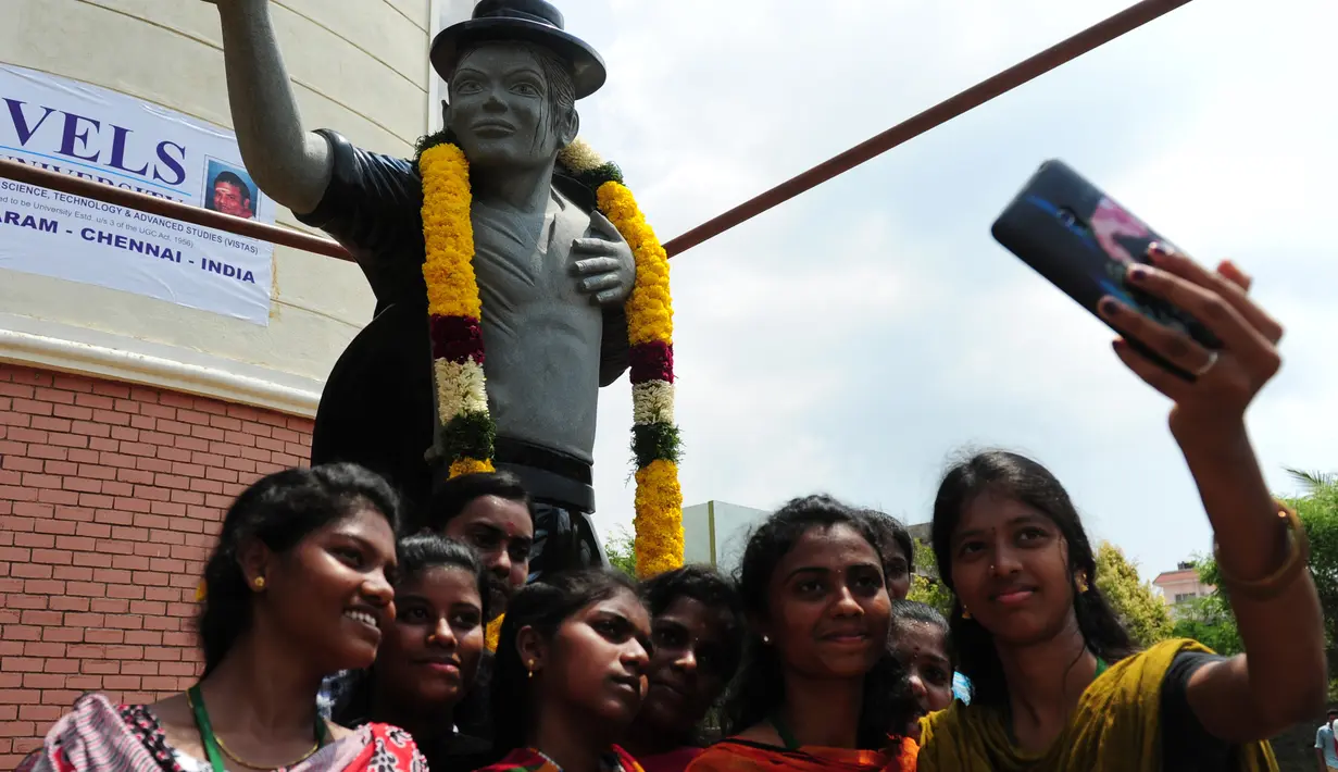 Sejumlah pelajar mengambil foto bersama patung bintang pop AS Michael Jackson di Chennai, India, Kamis (7/4).Patung tersebut juga dikalungi oleh Varmala khas India. (Arun Sankar/AFP)