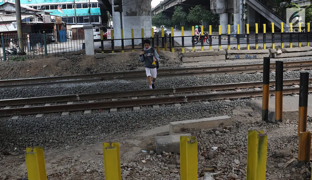 Seorang siswa menyeberangi perlintasan kereta api di Tanjung Barat, Jakarta, Senin (7/1). Meskipun sering terjadi kecelakaan dan dipasangi pagar, pejalan kaki tetap melompati pagar dari pada menggunakan fasilitas JPO. (Liputan6.com/Immanuel Antonius )