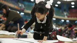 Seorang gadis kecil ikut ambil bagian kontes kaligrafi dalam merayakan tahun baru di Tokyo, Jepang, Selasa (5/1/2016). Lebih dari 3000 peserta menuliskan resolusi tahun baru di atas sebuah kanvas. (REUTERS / Thomas Peter)