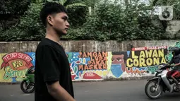 Warga melintasi mural bertema imbauan protokol kesehatan COVID-19 di kawasan Cakung Barat, Jakarta, Minggu (18/10/2020). Mural karya warga setempat tersebut bertujuan mengingatkan masyarakat akan pentingnya memakai masker, menjaga jarak, dan mencuci tangan. (merdeka.com/Iqbal S. Nugroho)