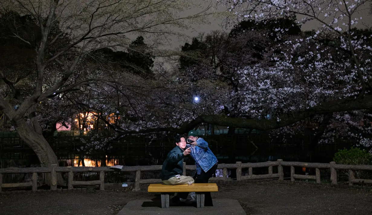 Sepasang kekasih berfoto di depan bunga sakura yang bermekaran saat malam hari di Taman Inokashira di Tokyo, Jepang (29/3/2022). (AFP/Philip Fong)