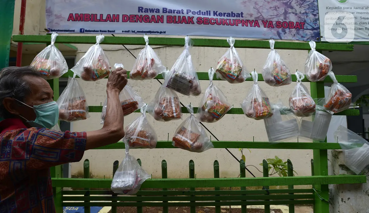 Warga mengambil sembako yang digantung di rak kayu sisi jalan di kawasan Rawa Barat, Jakarta Selatan, Kamis (14/5/2020). Selama masa pandemi COVID-19, pihak kelurahan dan masjid sekitar menyediakan paket berisi mi instan, telur, dan masker untuk warga yang membutuhan. (merdeka.com/Imam Buhori)