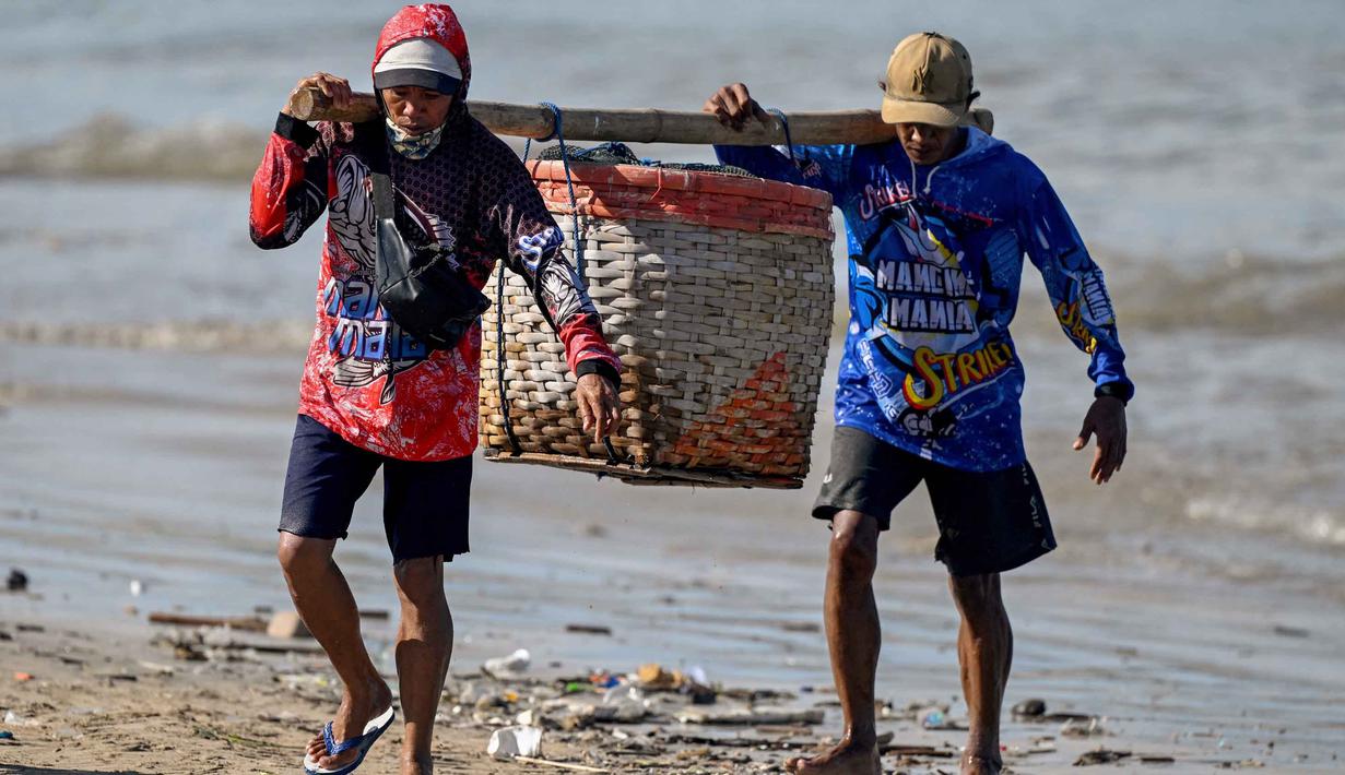 Sementara, perdagangan ikan di Bali berpusat pada perikanan tangkap (tuna, kakap) dan budidaya, dengan pelabuhan utama di Benoa, Kedonganan, dan Pengambengan. Tampak dalam foto, para pekerja membawa ikan setelah para nelayan menurunkan hasil tangkapan mereka dari perahu di pantai Kedonganan dekat Denpasar, Bali, pada Jumat 10 April 2026. (SONNY TUMBELAKA/AFP)