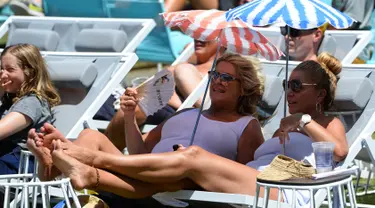 Dua penonton wanita duduk sambil membawa payung kecil menyaksikan serunya pertandingan tenis selama putaran pertama Australian Open 2017 di Melbourne, Australia (16/1). (AFP Photo/Greg Wood)