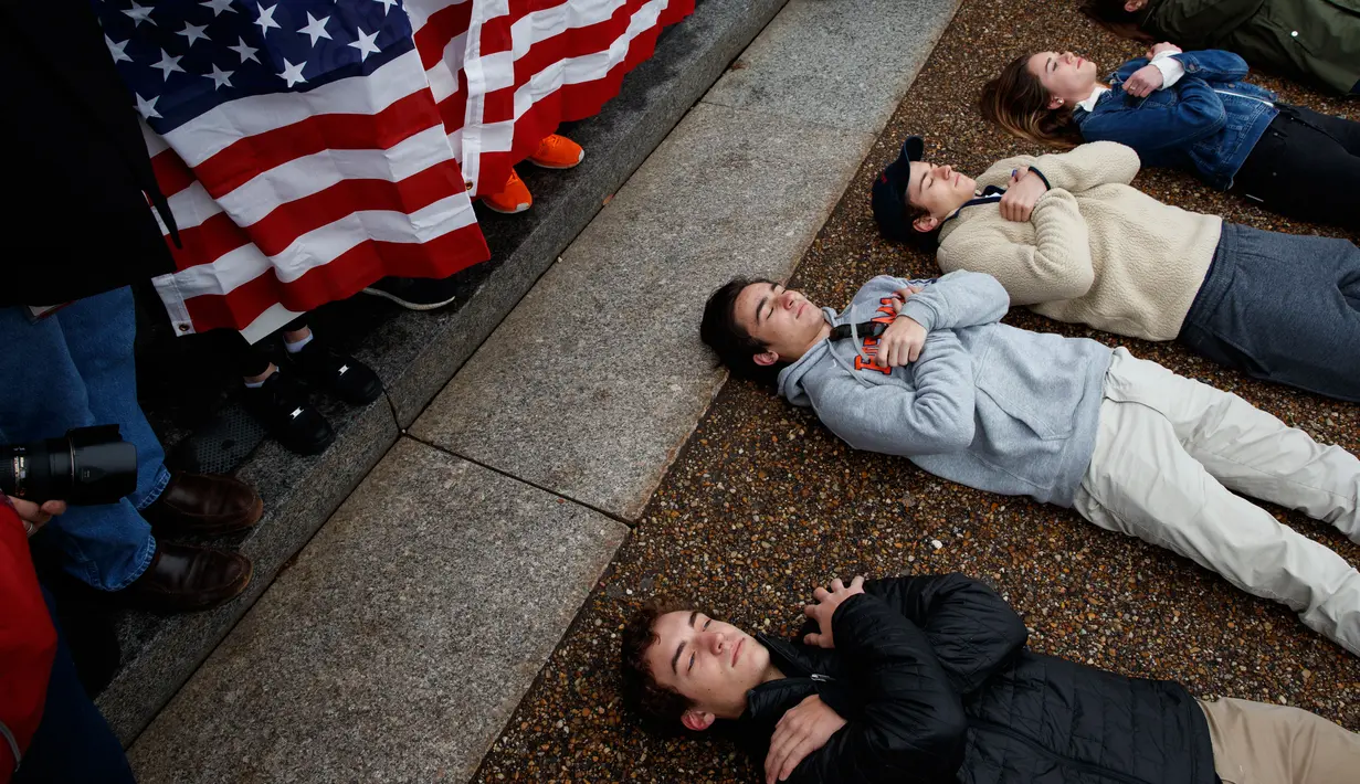 Pengunjuk rasa yang didominasi para siswa SMA berbaring di jalan depan Gedung Putih, Washington, Senin (19/2). Mereka berbaring dengan tangan bersilang di jalan basah di luar Gedung Putih. (AP Photo/Evan Vucci)