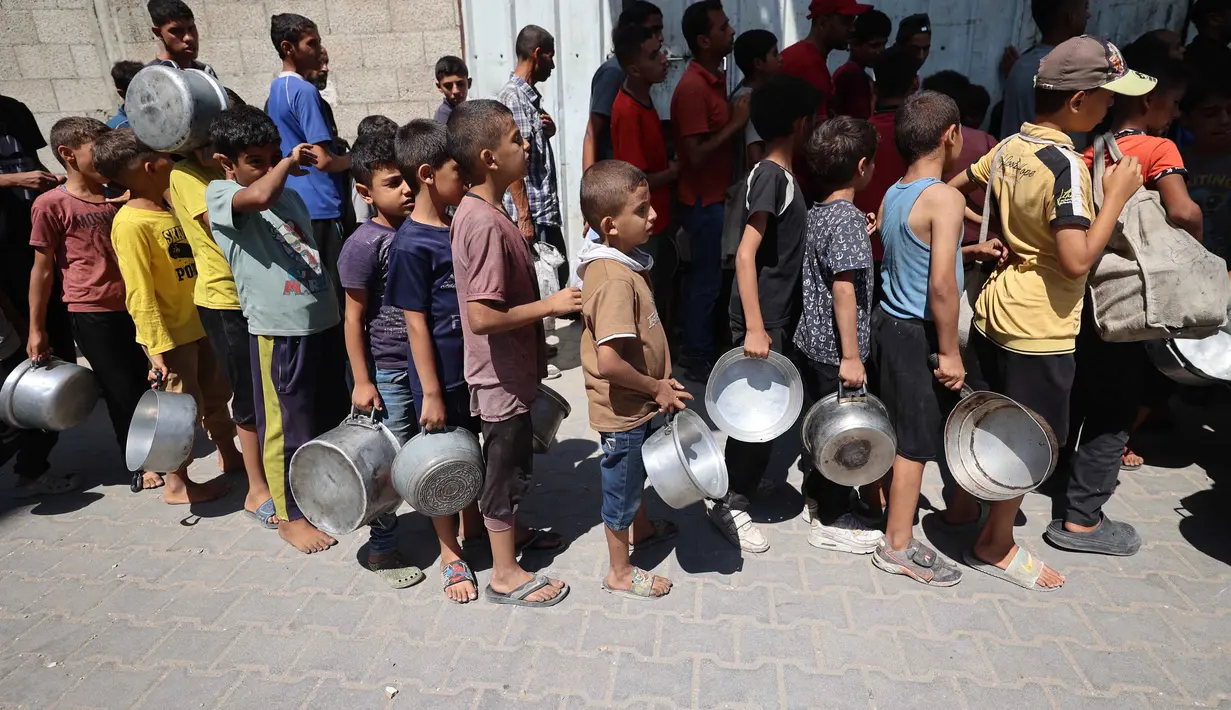Dua tahun sejak perang Israel–Hamas pecah pada 7 Oktober 2023, Jalur Gaza kini menghadapi krisis kemanusiaan terburuk dalam sejarah modern. Tampak dalam foto, anak-anak pengungsi Palestina mengantre untuk menerima makanan hangat dari dapur amal di kamp pengungsi Nuseirat di Jalur Gaza yang dikepung Israel pada 11 September 2025, di tengah bencana kelaparan yang dinyatakan PBB setelah hampir dua tahun perang. (Eyad BABA/AFP)