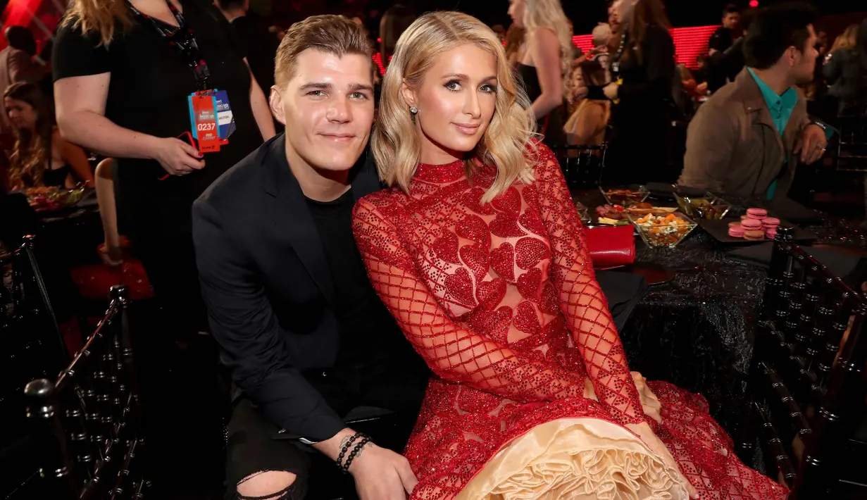 Paris Hilton dan tunangannya Chris Zylka duduk bersama saat menghadiri iHeartRadio Music Awards 2018 di Inglewood, California (11/3). Paris Hilton tampil cantik mengenakan busana merah dan Chris Zylka tampil dengan jas hitam. (AFP Photo/Christopher Polk)
