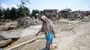 Sejumlah kendaraan roda empat teronggok dengan posisi terbalik atau tercebur ke parit. Tampak dalam foto, seorang korban membawa barang-barang bantuan di daerah yang terdampak banjir bandang di Aceh Tamiang, Sumatera, Indonesia, Jumat 5 Desember 2025. (AP Photo/Binsar Bakkara)