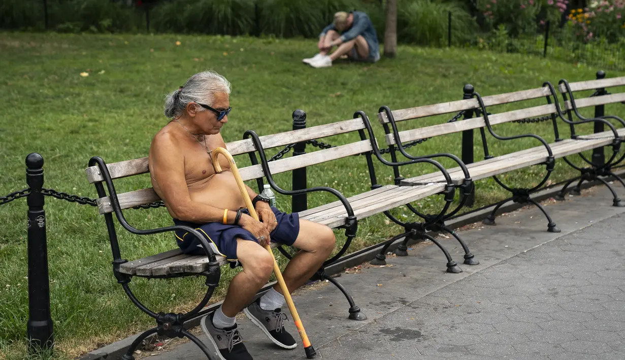 Seorang pria tanpa mengenakan baju beristirahat saat siang hari yang panas di Washington Square Park di New York City (17/7/2019). Panas terik bergerak ke daerah Kota New York, dengan suhu yang diperkirakan akan mencapai 100 derajat pada akhir pekan ini.  (AFP Photo/Drew Angerer)