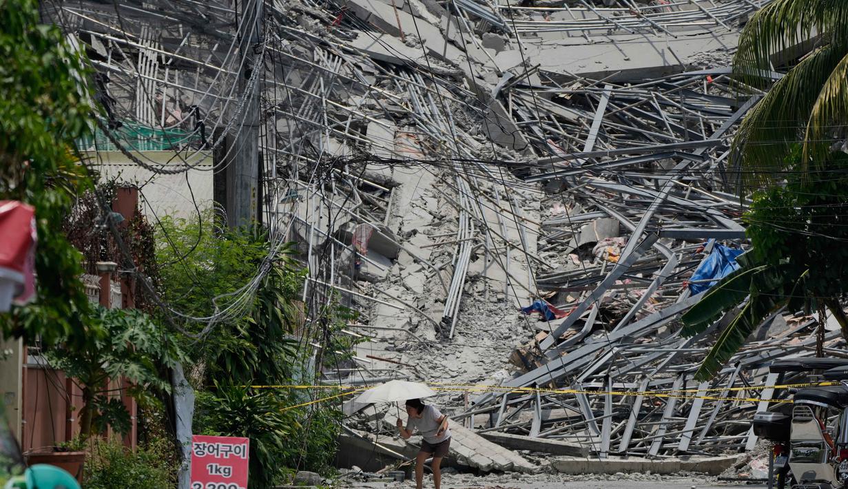 Seorang wanita berjalan di samping bangunan yang runtuh di kota Angeles, provinsi Pampanga, utara Manila, Filipina, Senin 25 Mei 2026. (AP Photo/Aaron Favila)