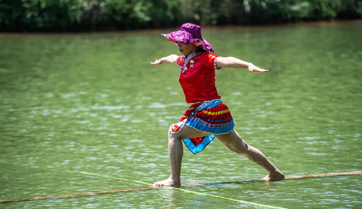 Seorang perempuan melakukan aksi meniti satu bambu di atas air di Chishui, Provinsi Guizhou, China pada 25 Juni 2020. Seni meniti satu bambu berasal dari Guizhou ini mengharuskan seseorang untuk berdiri atau duduk di atas sebatang bambu sembari melakukan gerakan keseimbangan. (Xinhua/Tao Liang)