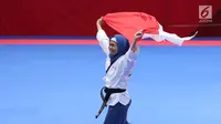 Atlet Taekwondo putri Indonesia, Defia Rosmaniar mengibarkan bendera Merah Putih saat merayakan kemenangan atas Salahshouri Marjan (Iran) pada Final Women Individual Poomsae di JCC, Jakarta, Minggu (19/8). (Liputan6.com/Helmi Fithriansyah)