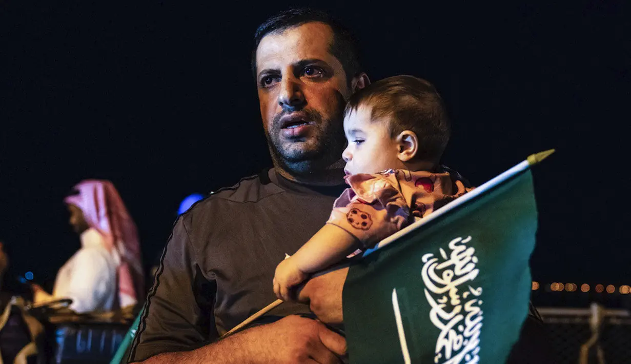 <p>Seorang pria menggendong seorang anak sambil membawa bendera Arab Saudi saat dievakuasi dari Sudan dan tiba di Pelabuhan Jeddah. (Saudi Ministry of Media via AP)</p>