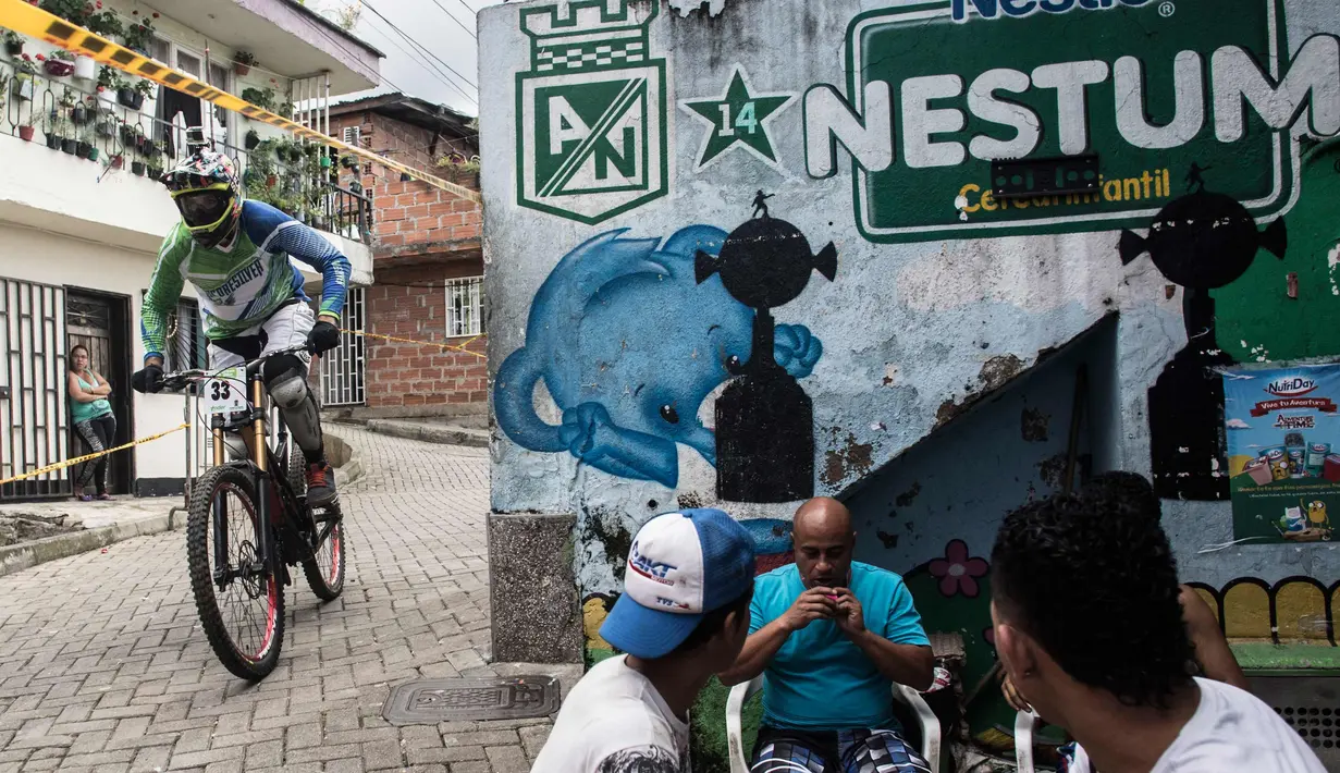 Pengendara sepeda melintas di dekat warga yang sedang berkumpul saat mengikuti balapan Urban Bike Inder Medellin di gubuk comuna 1 di Medellin, Antioquia department, Kolombia (19/11). (AFP Photo/Joaquin Sarmiento)