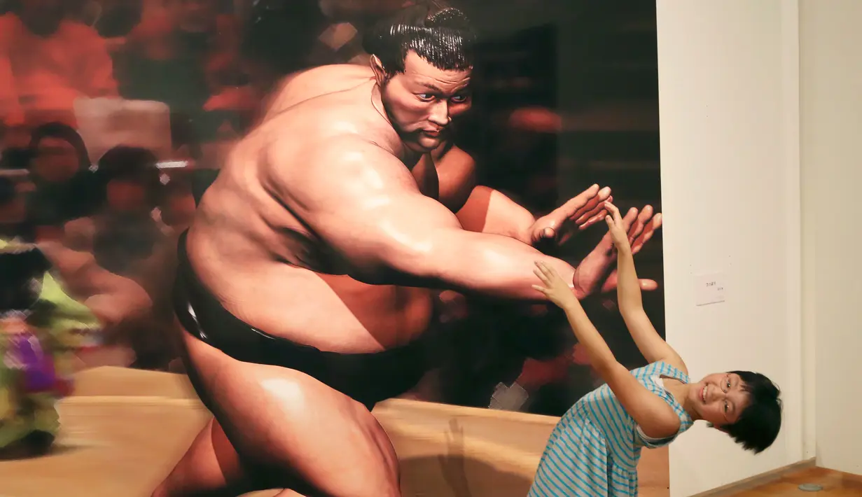 Seorang gadis berpose dengan gambar 3D pesumo pada pameran seni trik 3D karya seniman Jepang Masashi Hattori di Kawasaki, dekat Tokyo, Sabtu, (5/8). (AP Photo / Koji Sasahara)