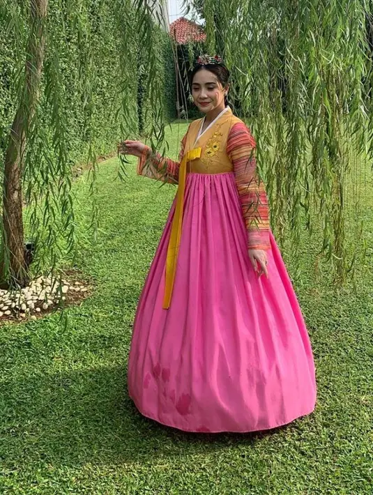 Nagita Slavina tampak elegan mengenakan hanbok dengan warna atasan kuning yang dipadukan dengan rok pinknya. Bordiran bunga di bagian depan membuat hanboknya semakin cantik. Ia pun menghiasi rambutnya dengan aksesori khas perempuan Korea Selatan. Dok Instagram/merryraffiahmad