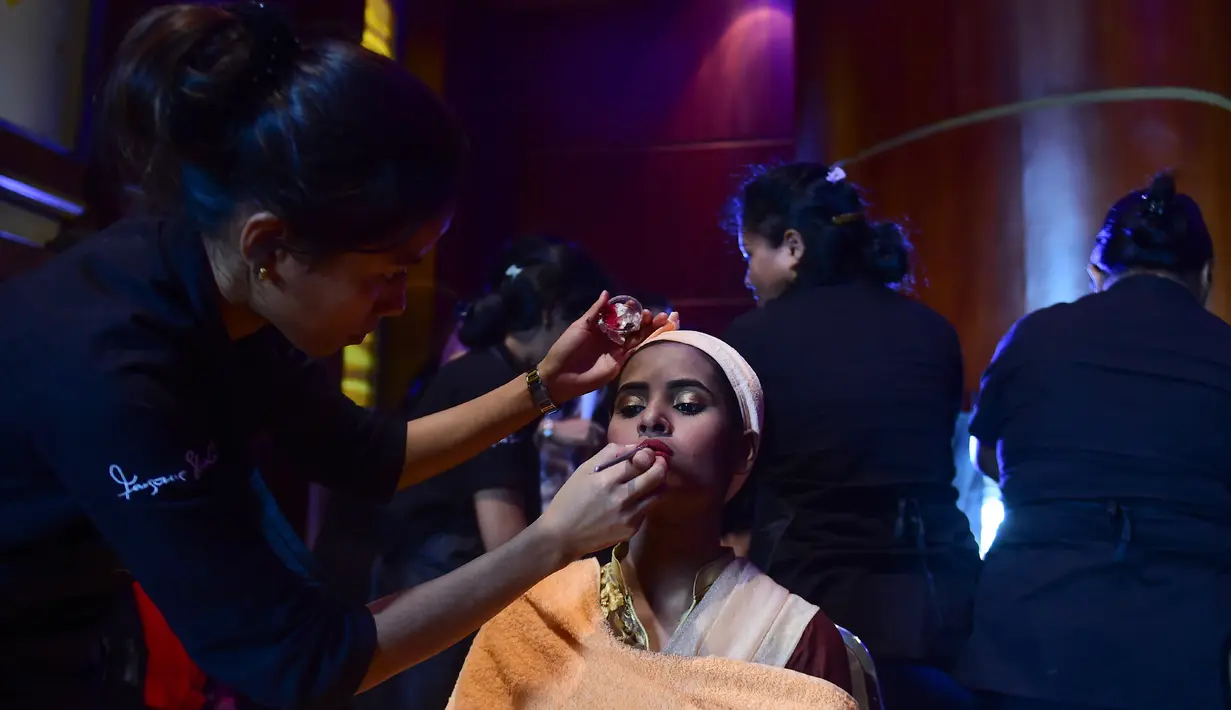 Penata rias mengaplikasikan make up ke wanita korban serangan cairan asam sebelum tampil pada pagelaran busana bertajuk "Beauty Redefined" di Dhaka, Bangladesh, 7 Maret 2017. Acara ini bertujuan mendefinisikan ulang konsep tentang kecantikan. (STR/AFP)