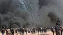 Para pengunjuk rasa Palestina berkumpul di depan ban yang terbakar saat aksi protes di perbatasan Gaza dengan Israel, Jumat (6/4). Tentara terus menembakkan gas air mata dan peluru tajam selama aksi berlangsung. (AP Photo/Adel Hana)