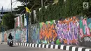 Pengendara melintasi jalur inspeksi Sungai Ciliwung di Jakarta, Kamis (27/12). Mural yang dibuat oleh beberapa komunitas tersebut menjadikan jalur inspeksi Sungai Ciliwung tampak lebih berwarna dan asri. (Liputan6.com/Immanuel Antonius)
