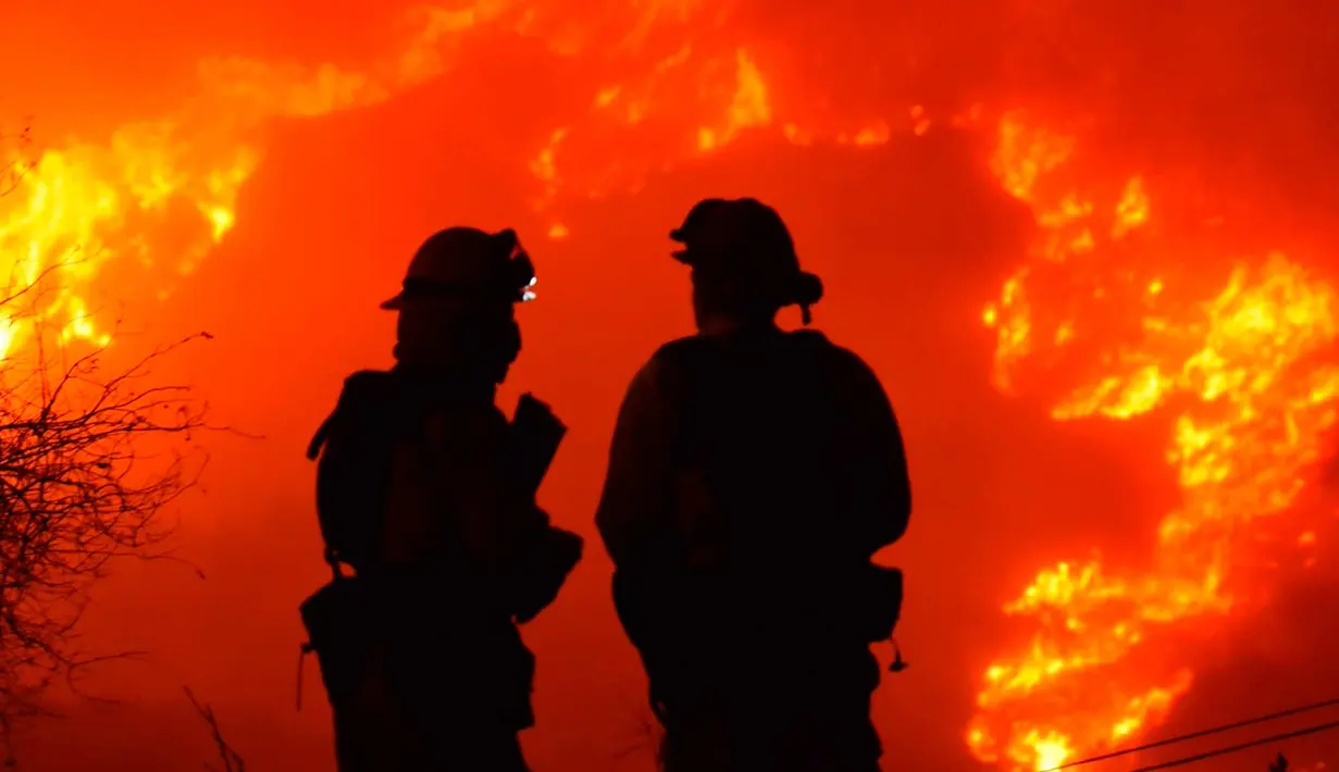 Dua petugas pemadam kebakaran mengecek api di atas Shepard Mesa Road di Carpinteria, California (10/12). Sejumlah warga di wilayah ini berhasil dievakuasi setelah api melalap permukiman mereka. (Mike Eliason/Santa Barbara County Fire Department via AP)