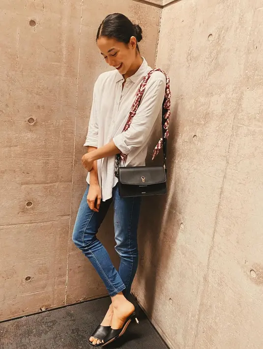 Kaus putih dipadukan dengan celana jeans menjadi pakaian yang tak pernah salah. Ia pun memadukan dengan sling bag berwarna hitam serta heels berwarna senada. (Liputan6.com/IG/@putrimarino)
