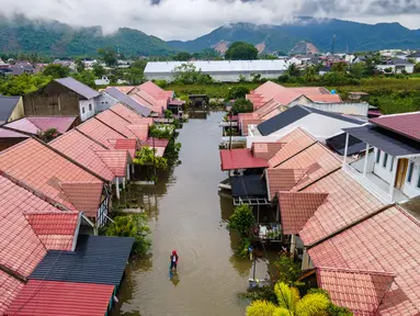Foto udara menunjukkan seorang pria melintasi banjir setelah hujan deras di permukiman Darul Imarah di pinggiran Banda Aceh pada Kamis 27 November 2025. Curah hujan tinggi yang dipicu siklon tropis menyebabkan sejumlah wilayah di Aceh Besar, termasuk Darul Imarah, terendam banjir. (CHAIDEER MAHYUDDIN/AFP)
