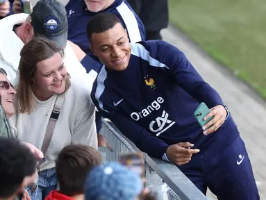 Penyerang timnas Prancis, Kylian Mbappe berswafoto dengan para penggemar di akhir sesi latihan di Stadion Home Deluxe Arena di Paderborn, Jerman, pada 13 Juni 2024. (FRANCK FIFE/AFP)