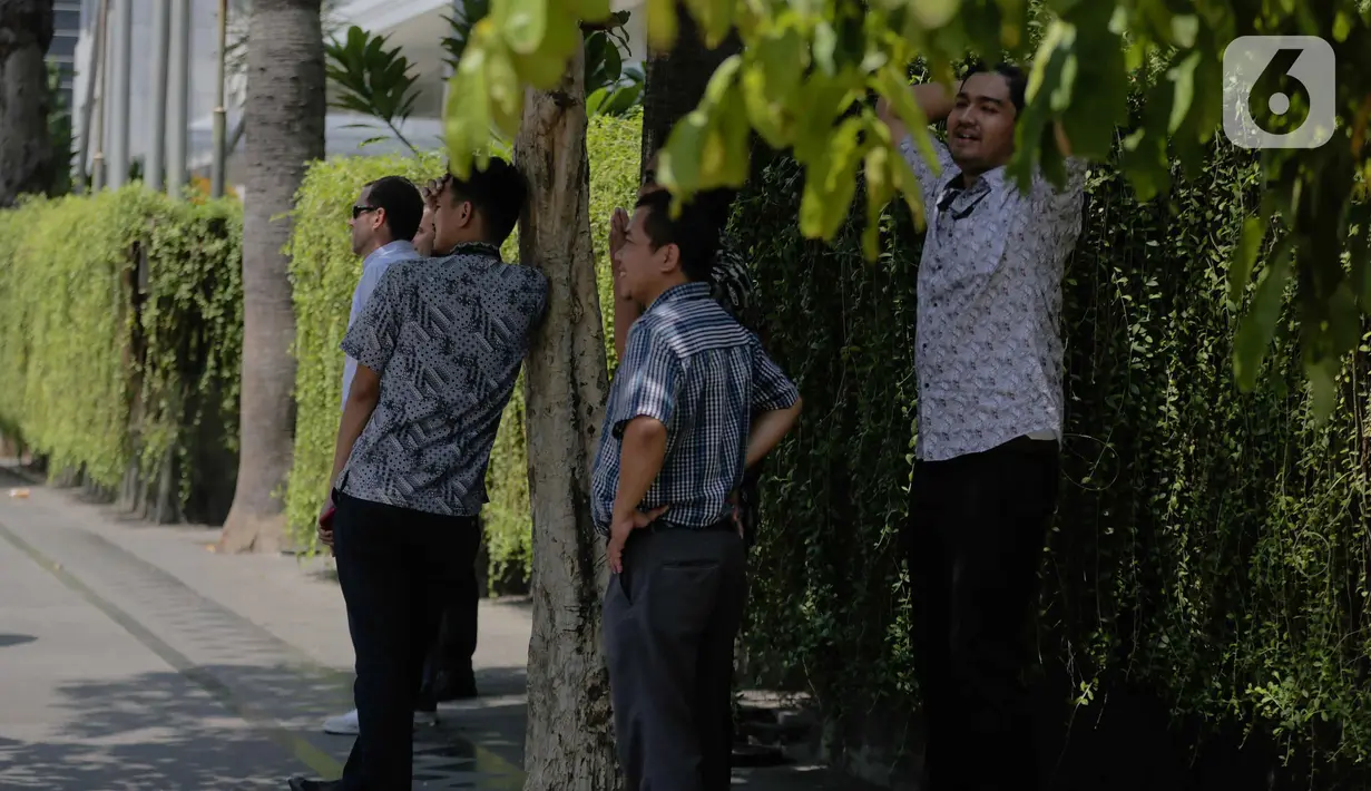 Sejumlah pria berdiri di bawah pohon selama gelombang panas di Jakarta, Selasa (22/10/2019).  BMKG memprediksi wilayah Indonesia akan mengalami panas selama kurang lebih satu minggu ini. Hal ini dikarenakan matahari yang berada dekat dengan jalur khatulistiwa. (Liputan6.com/Faizal Fanani)