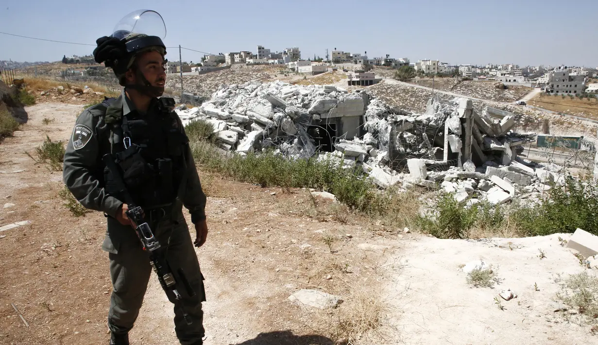 Seorang tentara Israel berjaga di depan bangunan Palestina yang telah dihancurkan di Tepi Barat (22/7/2019). Israel kembali menghancurkan sejumlah rumah Palestina yang dianggapnya dibangun secara ilegal di selatan Yerusalem. (AFP Photo/Hazem Bader)