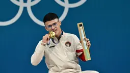Peraih medali emas dari Indonesia, Rizki Juniansyah, berpose di podium setelah pertandingan angkat besi kelas -73kg putra selama Olimpiade Paris 2024 di South Paris Arena di Paris, pada 8 Agustus 2024. (Miguel MEDINA/AFP)