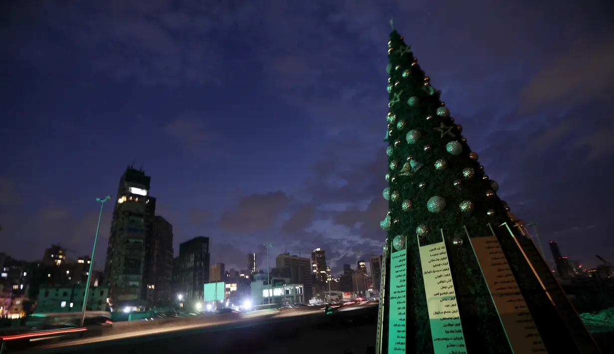Sebuah pohon Natal dengan daftar nama korban yang tewas dalam insiden ledakan di Pelabuhan Beirut terlihat di dekat silo gandum yang rusak di Beirut, Lebanon (22/12/2020). Pohon Natal ini didirikan juga bentuk penghormatan kepada mereka yang tewas dalam ledakan tersebut. (Xinhua/Bilal Jawich)