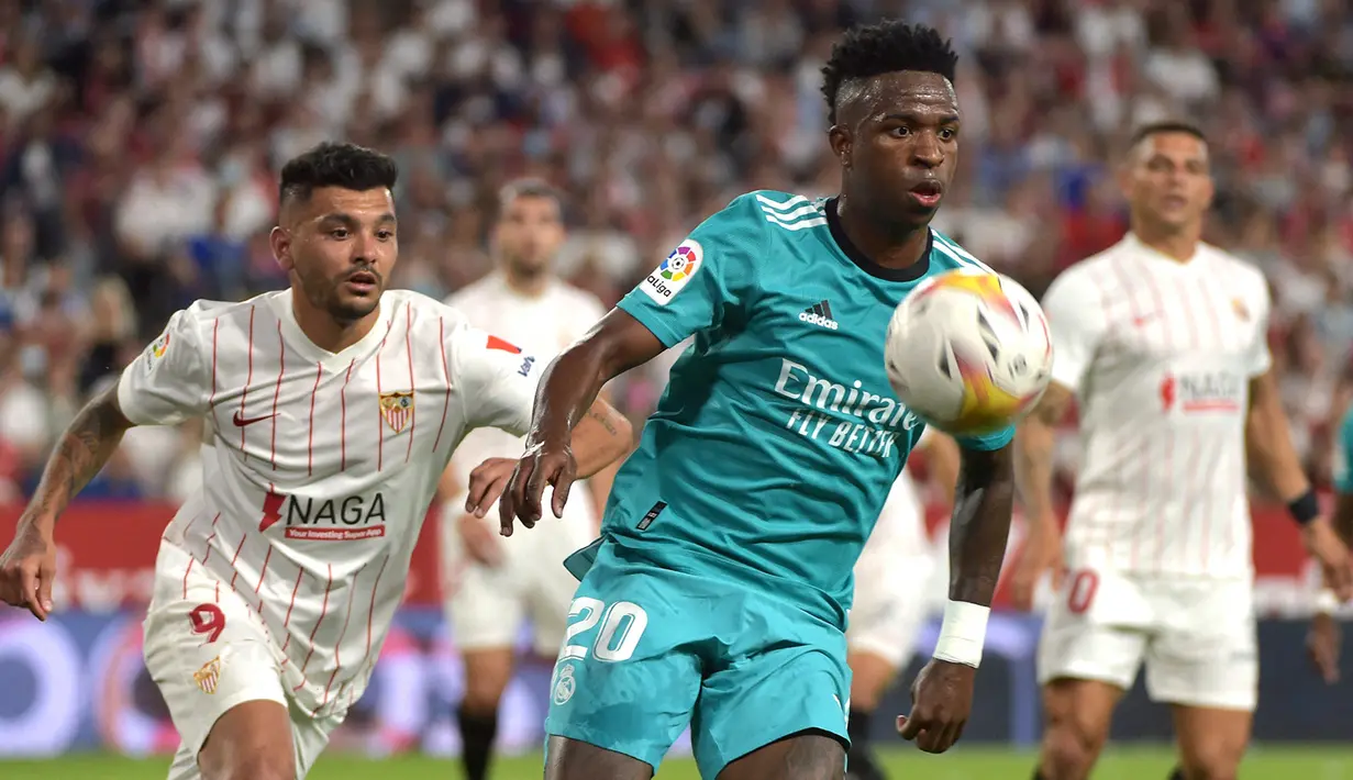 Penyerang Real Madrid Vinicius Junior (kanan) bersaing dengan pemain depan Sevilla Jesus Manuel Corona alias Tecatito pada lanjutan Liga Spanyol di stadion Ramon Sanchez Pizjuan, Senin (18/4/2022) dini hari WIB. Real Madrid sukses menaklukkan Sevilla 3-2. (CRISTINA QUICLER / AFP)