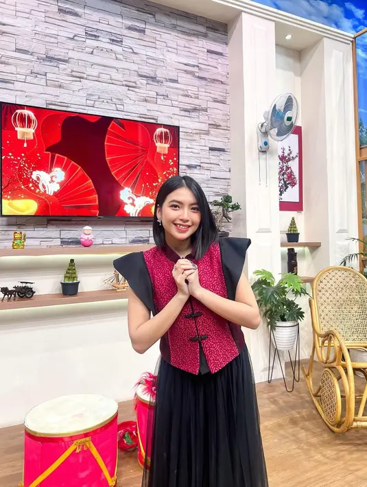Gracia JKT48 unggah foto outfit Imlek di sela-sela syuting. Ia kenakan atasan cheongsam hitam merah dengan lengan segitiga dan rok tulle yang manis [@jkt48.gracia]