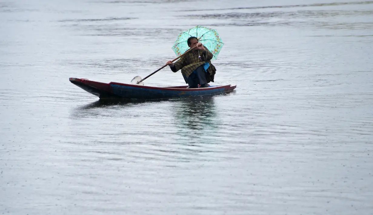 Seorang awak perahu Kashmir mengangkut penumpang saat hujan di Danau Dal di Srinagar (20/3). (AFP Photo/Tauseef Mustafa)