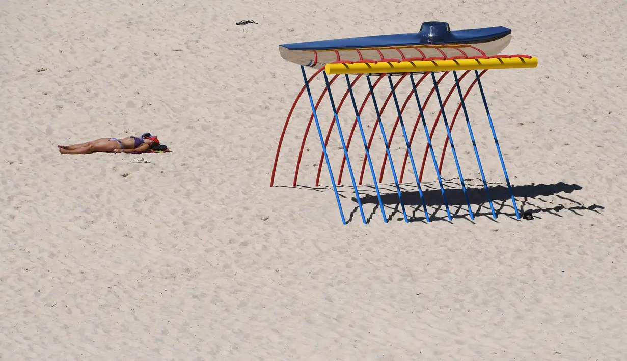 Pengunjung berjemur di dekat sebuah patung yang dipamerkan di pantai Bondi hingga Tamarama di Sydney, Rabu (19/10). Pameran yang bernama ‘Sculpture by the sea’ merupakan pameran patung tahunan diluar ruangan yang terbesar di Australia. (PETER PARKS/AFP)