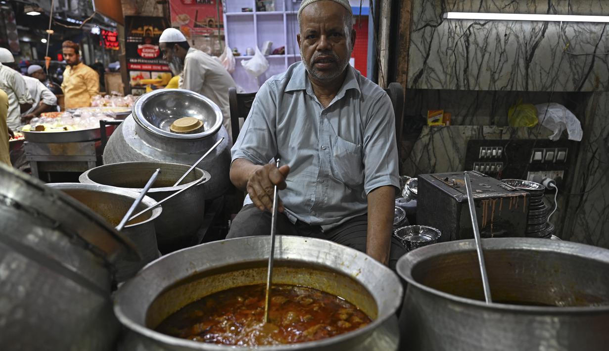 Dalam gambar pada 3 April 2022, penjaga toko berpose dengan hidangan di sebuah restoran di pasar pada hari pertama Ramadhan di kawasan tua Delhi, India. Masjid dan jalan-jalan pasar penuh dengan keramaian malam, tergoda oleh aroma manisan manis untuk berbuka puasa. (Money SHARMA/AFP)