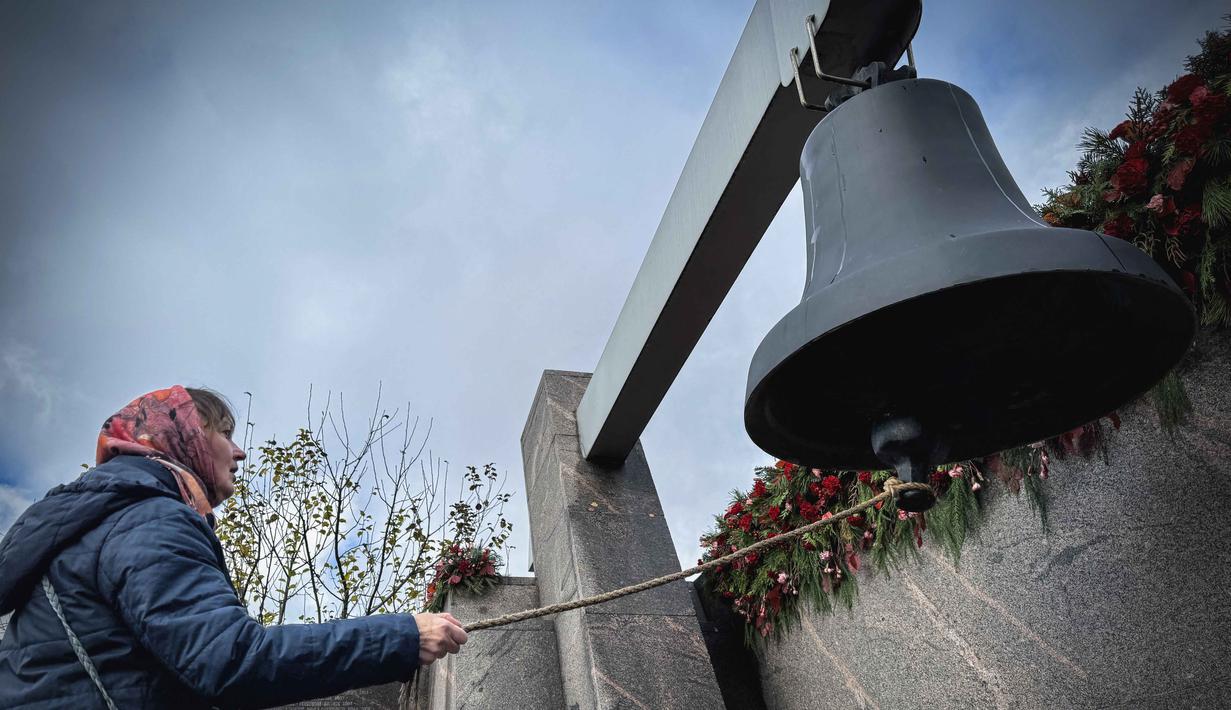 Seorang perempuan membunyikan lonceng saat mengunjungi monumen peringatan bagi para korban represi politik di Butovo, di luar Moskow, pada Kamis 30 Oktober 2025, menandai hari peringatan. Untuk diketahui, situs ini merupakan kuburan massal bagi lebih dari 20.000 orang yang dieksekusi secara rahasia selama kampanye pembersihan politik Stalin antara tahun 1937 dan 1938. (Nikita BORISSOV/AFP)