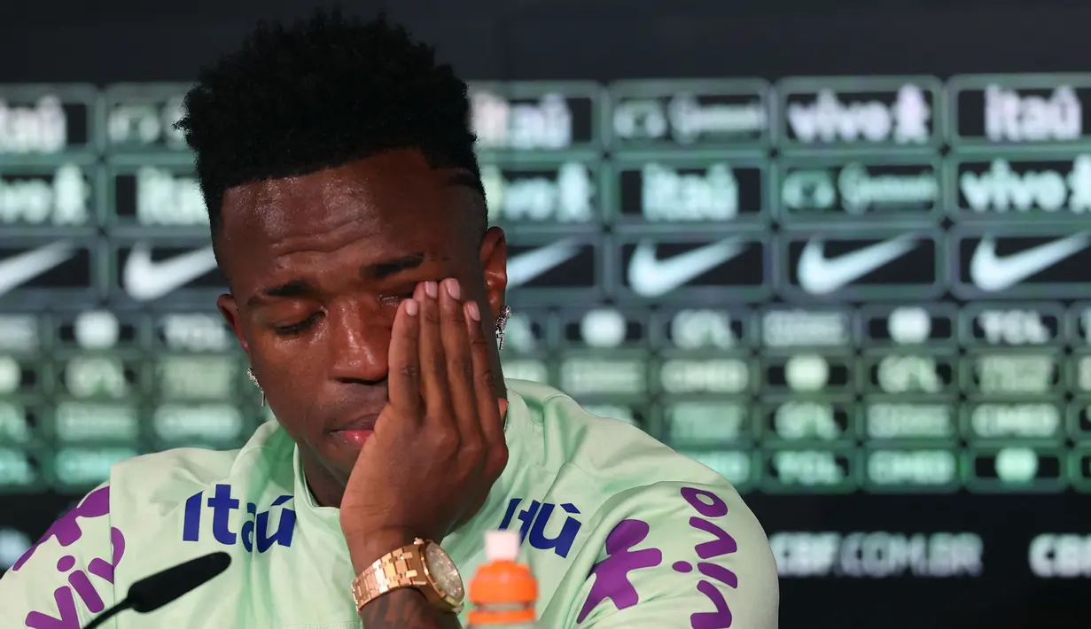 Pemain Brasil, Vinicius Jr menyeka air mata saat konferensi pers menjelang laga persahabatan melawan Spanyol di tempat latihan Ciudad Real Madrid di Valdebebas, pinggiran Madrid, pada 25 Maret 2024. Laga tersebut memiliki slogan "Satu Kulit" untuk membantu memerangi rasisme. (AFP/Pierre-Philippe Marcou)