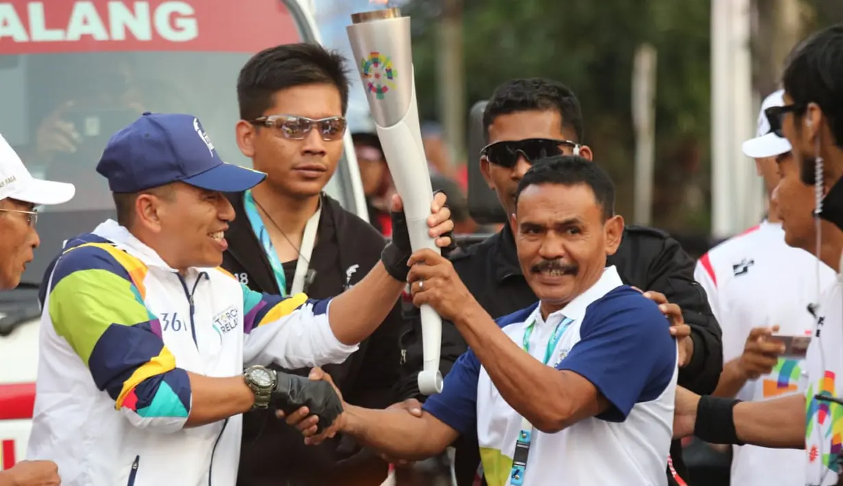 Petinju legendaris Indonesia, Nico Thomas, membawa obor Asian Games XVIII saat melintas di Kota Malang, Jawa Timur, Jumat (20/7/2018). Sebanyak 53 kota di Indonesia akan dilalui oleh obor Asian Games. (Bola.com/Aditya Wani)