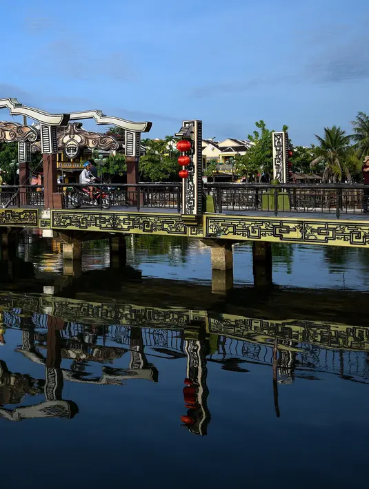 <p>Gambar pada 14 September 2019 menunjukkan turis melintasi jembatan An Hoi di seberang sungai Thu Bon, kota tua Hoi An, Vietnam. Kota Tua Hoi An merupakan destinasi wisata yang cukup populer di Vietnam, didukung oleh statusnya sebagai salah satu Unesco World Heritage Site. (Manan VATSYAYANA/AFP)</p>