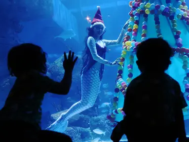 Anak-anak menyaksikan penyelam berkostum putri duyung di dalam air yang dihiasi pohon natal di Jakarta Aquarium dan Safari, Mal Neo Soho, Grogol, Jakarta, Kamias (24/12/2020). Pertunjukan tersebut untuk mengisi libur Natal dan Tahun Baru 2021. (Liputan6.com/Angga Yuniar)