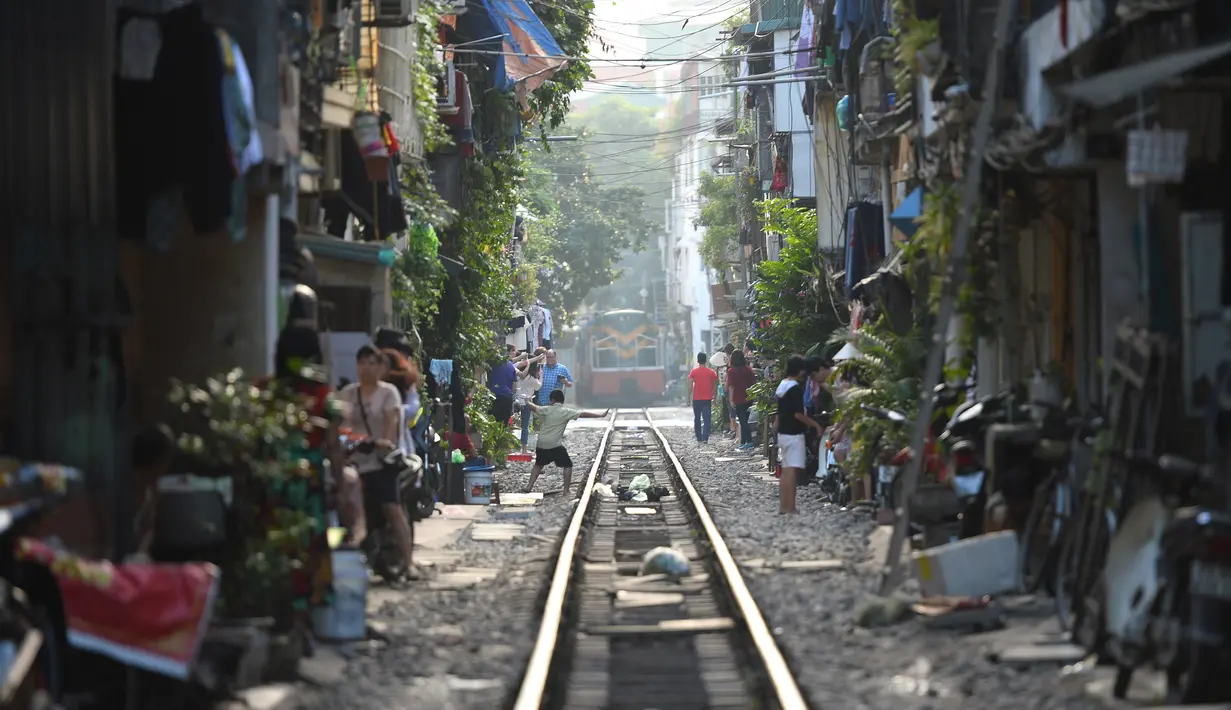 Gambar pada 21 Oktober 2018, rangkaian kereta api melewati jalur kereta yang melintasi kawasan permukiman di Hanoi, Vietnam. Rel yang selesai dibuat oleh Prancis pada tahun 1930an itu berada di tengah bangunan rumah dan pertokoan. (Nhac NGUYEN/AFP)