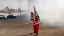 Pengunjuk rasa berkostum sinterklas atau Santa Claus memegang bendera Palestina sambil menutup hidungnya saat pasukan Israel menembakkan gas air mata dalam demonstrasi di Bethlehem, Tepi Barat, 23 Desember 2017. (AP/Nasser Shiyoukhi)