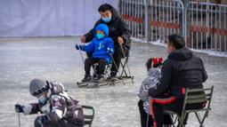 Seorang pria dan anak-anak menggunakan kursi yang dimodifikasi untuk meluncur melintasi es dalam kolam di taman umum saat pekan liburan Tahun Baru Imlek di Beijing, China, Kamis (26/1/2023). (AP Photo/Mark Schiefelbein)