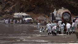 Petugas kebersihan bekerja untuk mengeluarkan minyak dari Pantai Cavero di Callao, Peru, 26 Januari 2022. Pembersihan Pantai Cavero dari tumpahan minyak kapal tanker Mare Doricum yang dihantam gelombang akibat letusan gunung berapi Tonga masih terus dilakukan. (Cris BOURONCLE/AFP)