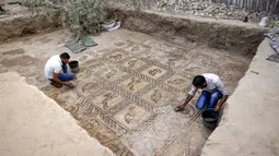 Dua orang pria membersihkan mosaik era Bizantium yang ditemukan di Bureij, Jalur Gaza, Palestina, 18 September 2022. Petani Palestina, Salman al-Nabahin mengatakan dia dan putranya sedang menggali tanah ketika mereka menemukan relik tersebut. (MOHAMMED ABED/AFP)