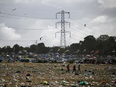 Penonton festival membawa barang-barang mereka saat berjalan melintasi lapangan yang dipenuhi sampah di akhir festival Glastonbury di desa Pilton di Somerset, barat daya Inggris, pada 26 Juni 2023. (AFP/Oli Scarff)