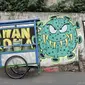 Pedagang melintasi mural bertema imbauan protokol kesehatan COVID-19 di kawasan Cakung Barat, Jakarta, Minggu (18/10/2020). Mural karya warga setempat tersebut bertujuan mengingatkan masyarakat akan pentingnya memakai masker, menjaga jarak, dan mencuci tangan. (merdeka.com/Iqbal S. Nugroho)