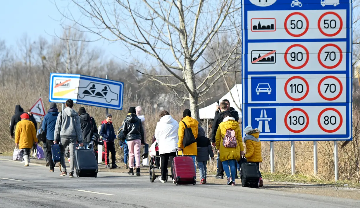 Keluarga Ukraina yang melarikan diri dari konflik di negara mereka sehari setelah Rusia melancarkan serangan militer berjalan dengan barang bawaan mereka setelah melintasi perbatasan Hungaria-Ukraina dekat Beregsurany, Hungaria (25/2/2022). (AFP/Attila Kisbenedek)